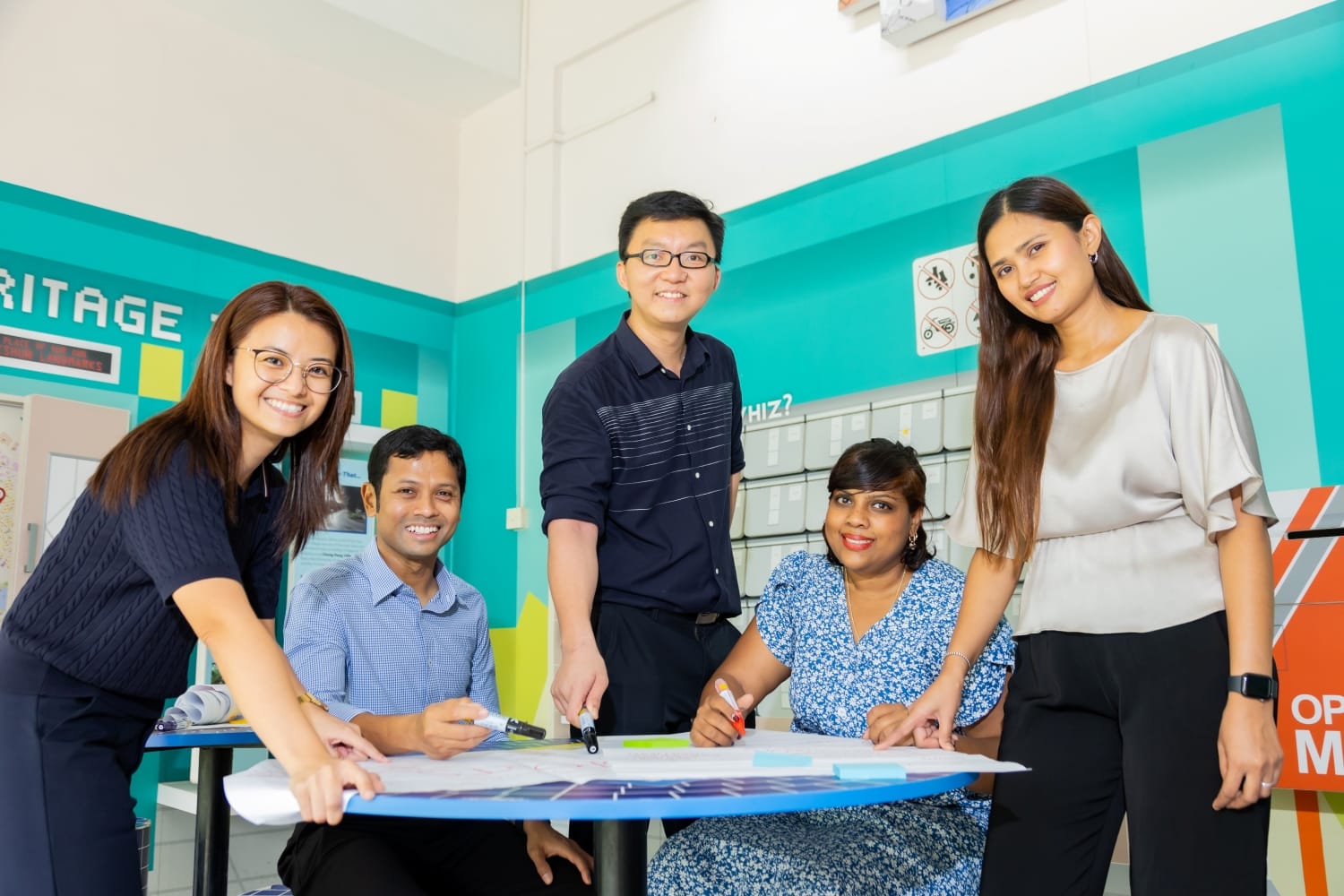 A group of 5 teachers posed around the table, some seated some standing